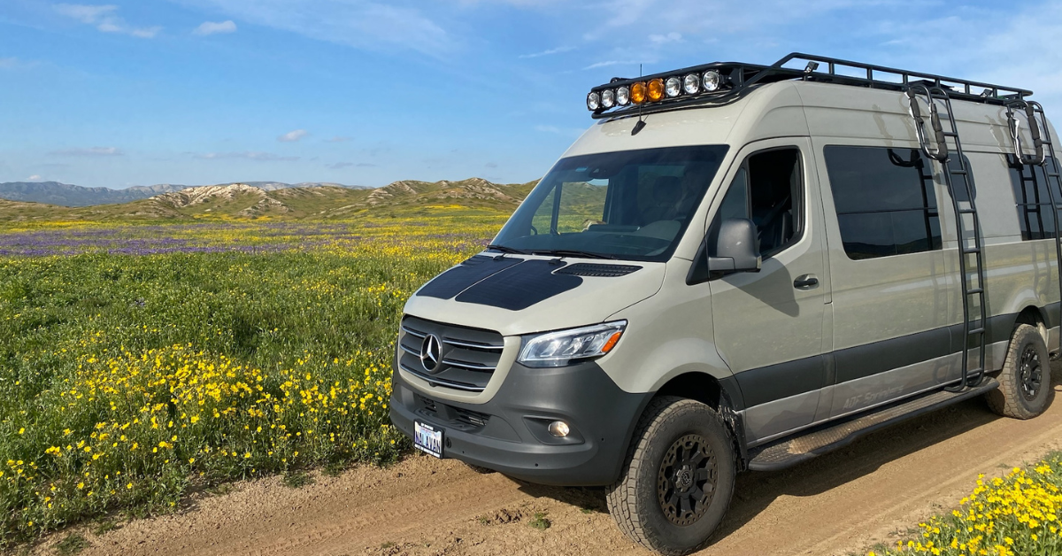 A Mercedes all wheel drive sprinter van on a dirt road with flowers
