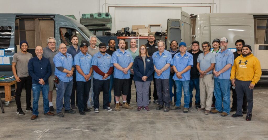 a group of people lined up and posing for a photo in a van conversion facility