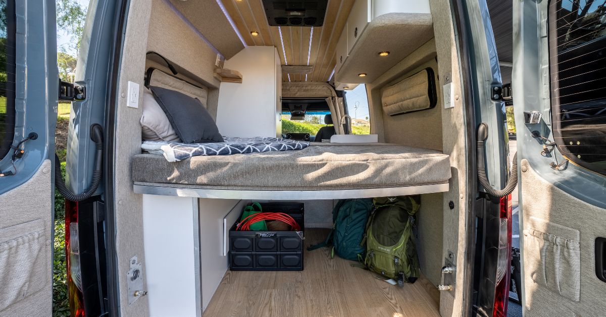 the back of a campervan with a platform bed and gear underneath